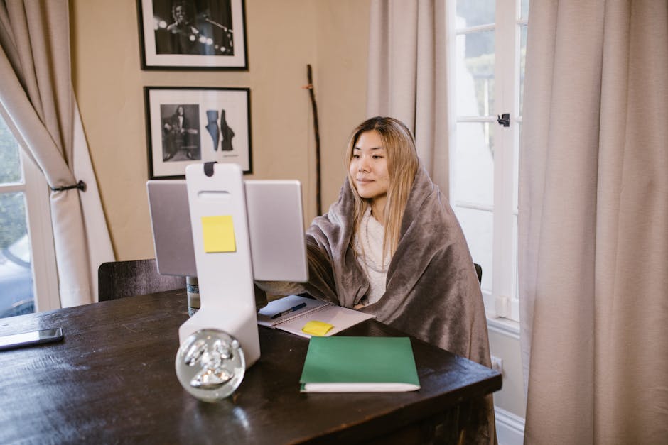 A woman wrapped in a blanket attending an online class at home using a computer