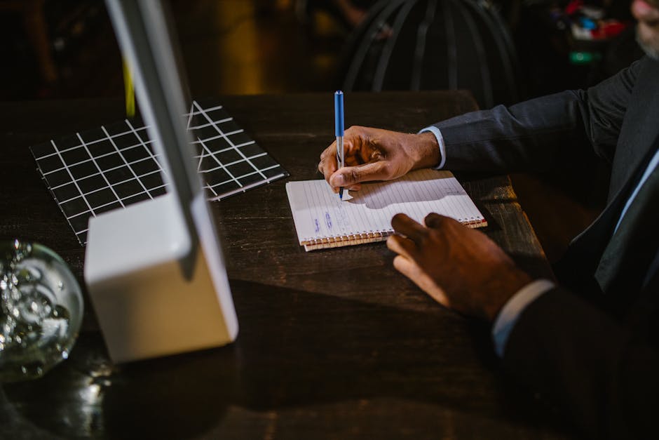 A businessman in a suit writing notes on a notebook at a desk, suggesting a professional office environment