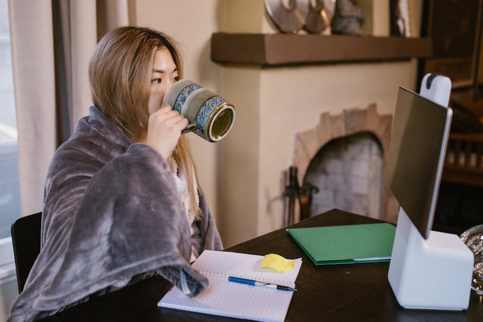 Adult woman sipping coffee while working remotely at home, with a cozy setup